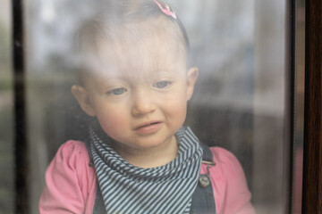 Sad baby girl staring out the window. Stay at home quarantine coronavirus pandemic prevention.