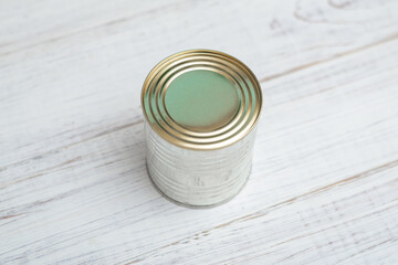 Closed metal can of canned food on a white wooden background.