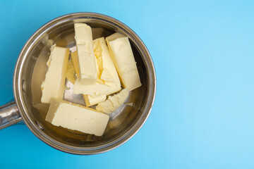 Chopped pieces of butter milk butter in a saucepan on a blue background. Preparing for melting.
