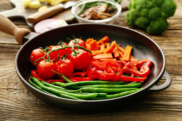 Frying pan with tasty vegetables on wooden background