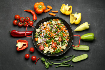 Composition with frying pan, tasty vegetables and chicken on dark background