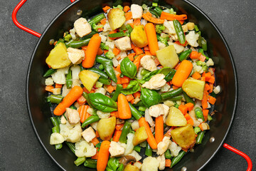 Frying pan with tasty vegetables and chicken on dark background, closeup
