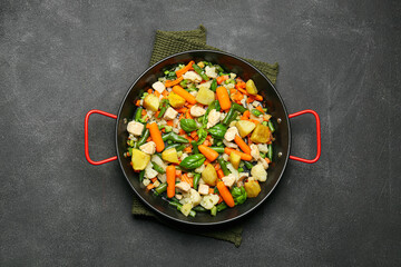 Frying pan with tasty vegetables and chicken on dark background