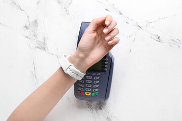 Female hand with smart watch and payment terminal on light background