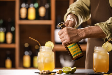 Bartender opening bottle of fresh ginger beer on table in bar