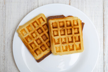 Freshly cooked Belgian waffles on a white plate on a light wooden background.