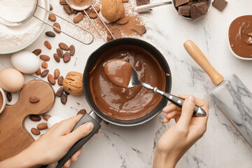 Woman cooking tasty melted chocolate on table in kitchen