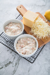 Typisches DDR Würzfleisch Ragout Fin mit geriebenen Gouda Käse in Auflaufform Schale und Zitrone auf Abkühlgitter und Marmor Hintergrund hell