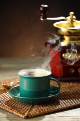 Cup of hot coffee and grinder on wooden background