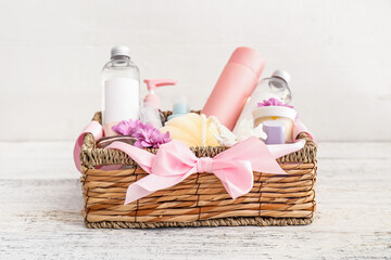Gift basket with cosmetics on light wooden background