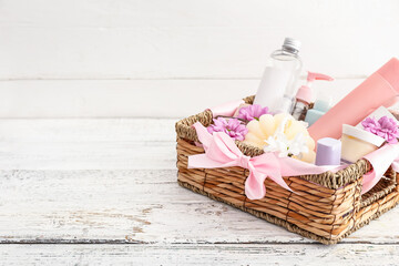 Gift basket with cosmetics on light wooden background