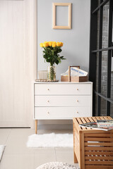 Vase with beautiful yellow roses on chest of drawers in interior of hall