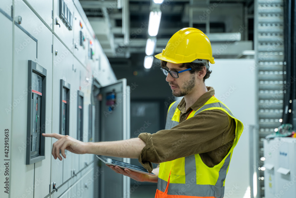 Poster portrait of electrician engineer use tablet computer taking notes at control room in factory.