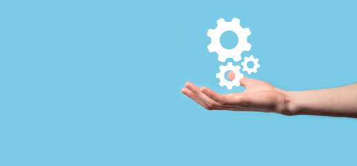 Male hand holding cog gears icon ,mechanism icon on virtual screens on blue background. Automation Software Technology Process System Business concept. Banner