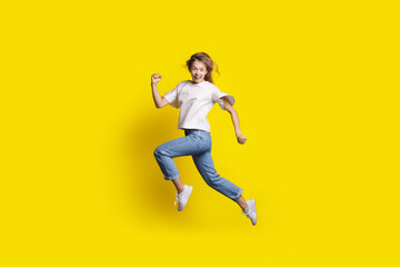 Crazy woman is jumping in a yellow studio wall smiling at camera gesturing a run