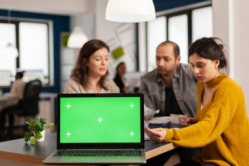 Fototapeta na wymiar Laptop with green screen chroma key display. mock up desktop ready for presentation placed on desk while business people work in background. Group of employees using notebook with isolated monitor