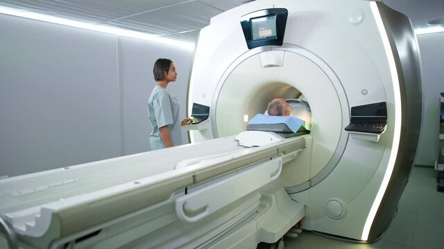 Magnetic resonance imaging in the modern hospital, young woman doctor performs a magnetic tomographic examination of a elderly man, MRI, modern technologies in medicine, end of the procedure.