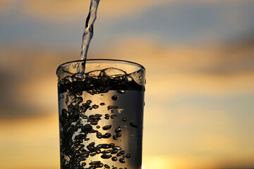Clean water pouring into drinking glass on sunset blurred background. Concept of health and...