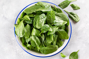 Fresh organic baby spinach leaves on a plate on a light concrete background, top view. Healthy food...