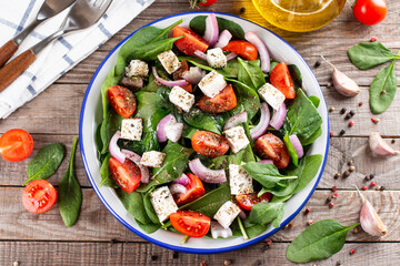 Fresh vegetables salad from spinach, tomato, feta cheese, onion in plate on a wooden table. Top view