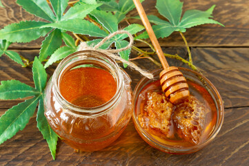 Cannabis leaves, Marijuana, and fresh organic pure honey in glass jar on wood table background. Honey CBD concept.