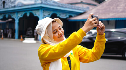 Asian female traveling taking selfies at the keraton solo wearing jilbab and analog camera