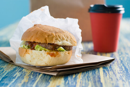 Burger With Beef Cutlet, Sauce, Salad And Coffee To Go In A Paper Cup Side View, Copy Space. Concept Of Food Delivery, Restaurant Operation During Quarantine Covid 19