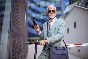 Senior business man with electric scooter in the city. Using smart phone.