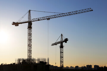 Silhouettes of construction cranes and buildings on sunrise background. Housing construction, apartment block in city