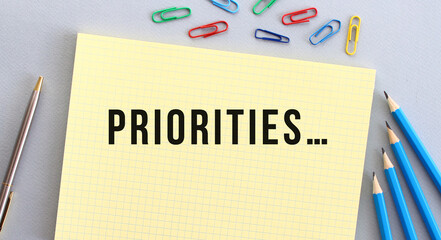 PRIORITIES text in notebook on gray background next to pencils, pen and paper clips.