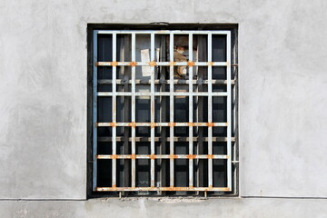 Rusted metal bars protection covering old broken window with safety glass and dilapidated cracked wooden frame mounted on grey old abandoned factory building wall at local industrial complex