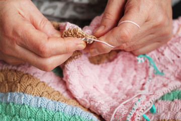 Female Senior Hands with wrinkles. The age hands of a woman with knitting needles knit a product, grandmother's hobby clothes are made by hand, knitting a colored sweater	