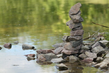 tower built of stones stacked on top of each other on the edge of a pond, green background with space for text