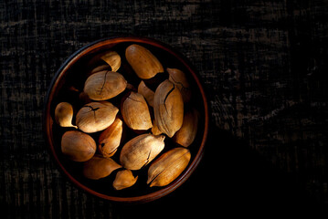 Pecan in a clay bowl on a shabby wooden board. Nuts in shell on an old black table. Contrasting dramatic light as an artistic effect. Copy space and free space for text near nuts.