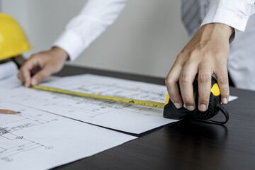 An engineer is using a tape measure to measure the plans of the house that he designs, the drafts...