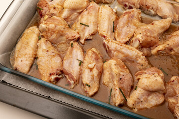 Raw chicken wings marinated with oil, pepper, chives, honey and spices on a baking tray.