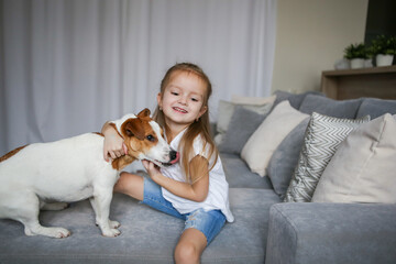 Happy child with a dog. Portrait of a girl with a pet. The child plays and hugs the puppy. Little girl and a puppy on the couch. Pet at home. Taking care of animals.