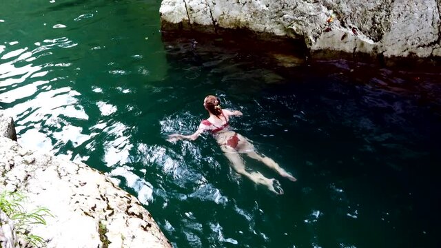 The girl swims in a turquoise deep river flowing between the rocks. Canyon white cliffs