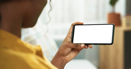 Close up of African American unrecognizable woman looking at smartphone with green screen and typing while sitting at home. Female holding black cellphone with chroma key in hand and tapping