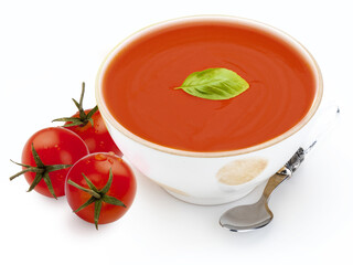 Bowl with tomato soup (gazpacho, tomatoes, basil leaf and spoon. Isolated on white background. Mediterranean diet of tomato, cucumber, peppers, olive oil, bread, garlic, vinegar and fresh basil leaf.