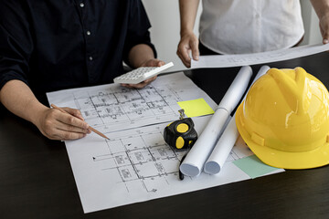 The architect was pressing the white calculator and there was an engineer standing there holding the floor plan. They are examining the draft blueprint for the designed building.
