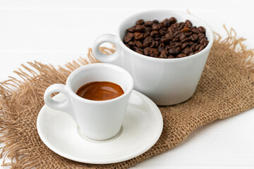 Cup of espresso coffee and coffee beans on white surface