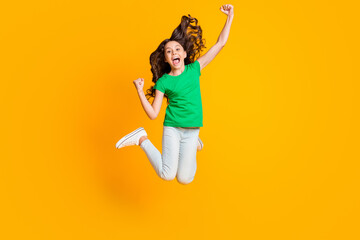 Full size photo of happy screaming happy excited little girl jumping raise fists in victory isolated on yellow color background