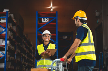 warehouse workers logistic team wearing hardhats to working in aisle between tall racks with packed...