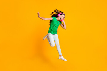 Fototapeta na wymiar Full size photo of happy screaming jumping girl enjoying listening music in headphones isolated on yellow color background