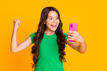 Photo of happy cheerful smiling funky crazy girl raise fist in victory use smartphone isolated on yellow color background