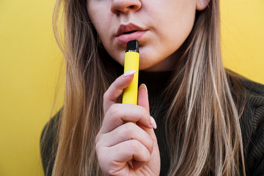 A young girl smokes disposable electronic cigarette. Bright yellow background
