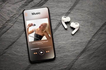 Music player on screen of mobile phone and wireless earphones on dark background