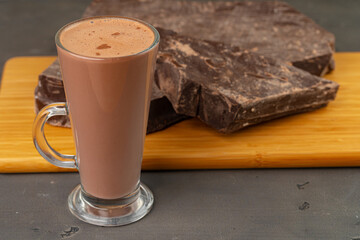 Hot cocoa drink in glass cup and chocolate bar on gray background
