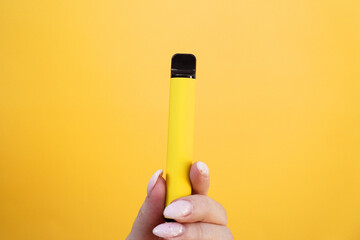 Yellow disposable electronic cigarette in female hand. Bright yellow background